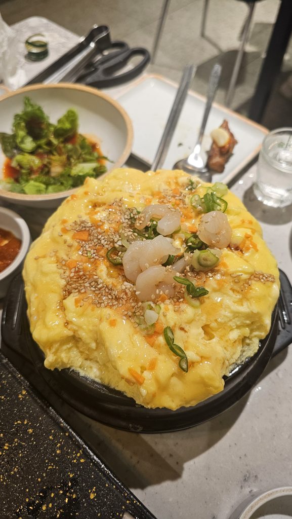 식당 뚝배기에 부풀어 오른 폭탄 계란찜 위에 새우와 쪽파, 깨가 올라간 사진